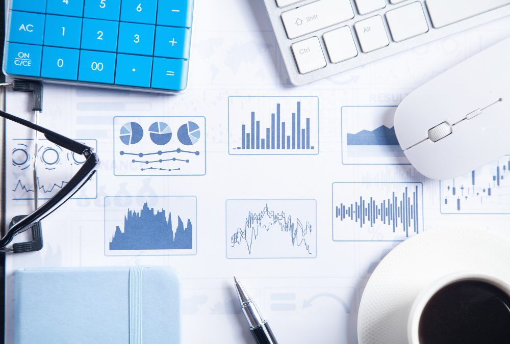Different types of graphs and charts, surrounded by computer peripherals, notebook, pen, coffee and glasses